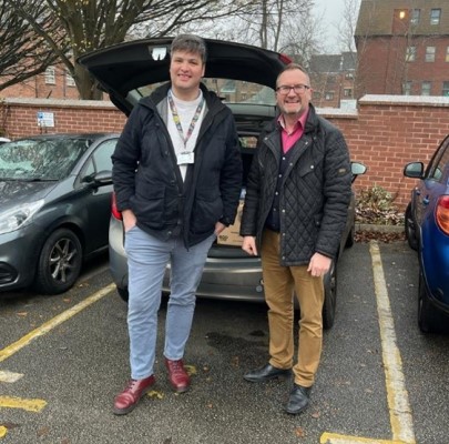 Two colleagues from Cornerstone Partnership standing in front of a car with a boot full of gifts
