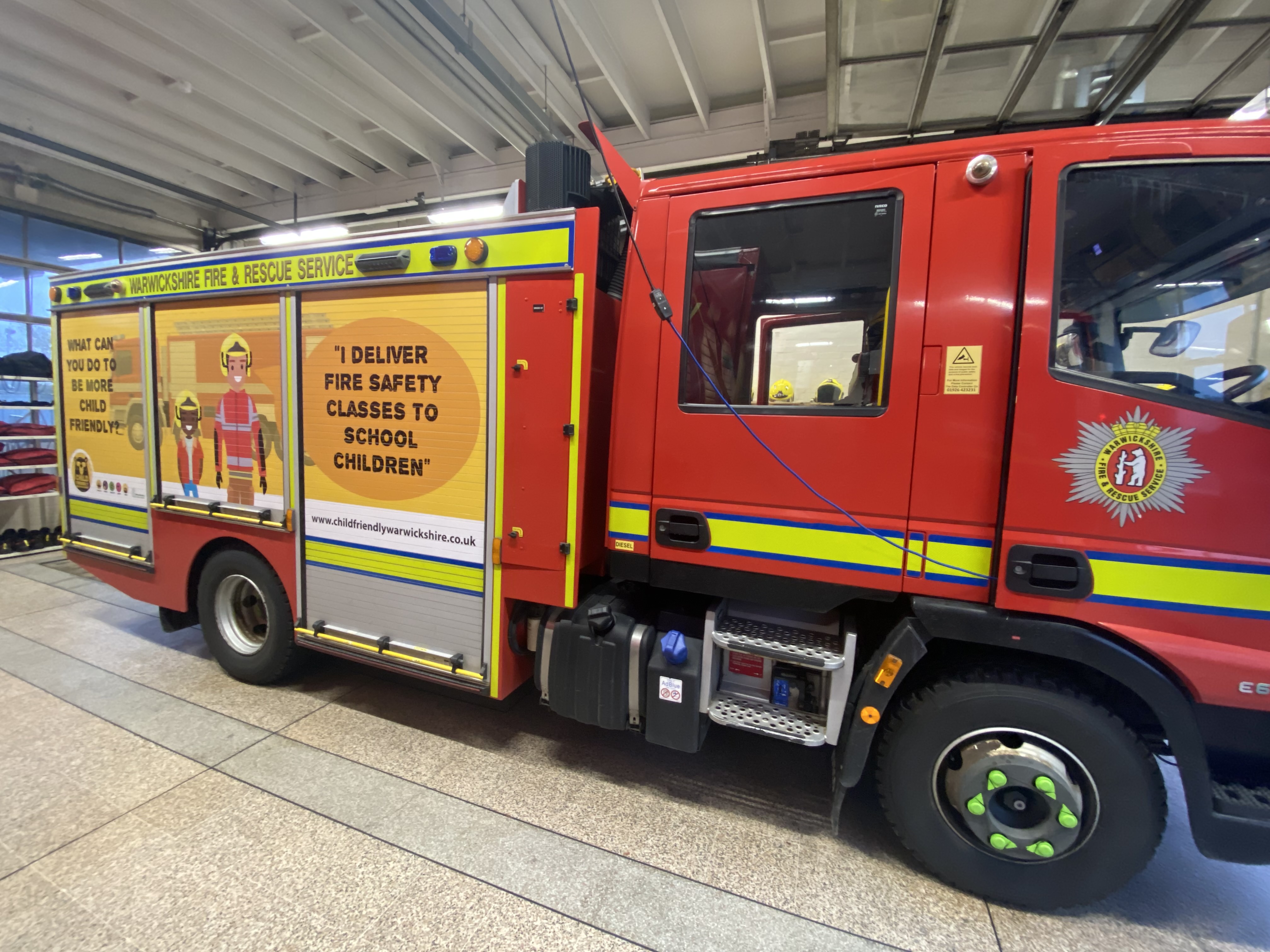 A fire engine in a station showing Child Friendly Warwickshire branding on the side
