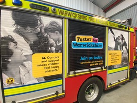 A fire engine in a station showing Fostering For Warwickshire branding on the side