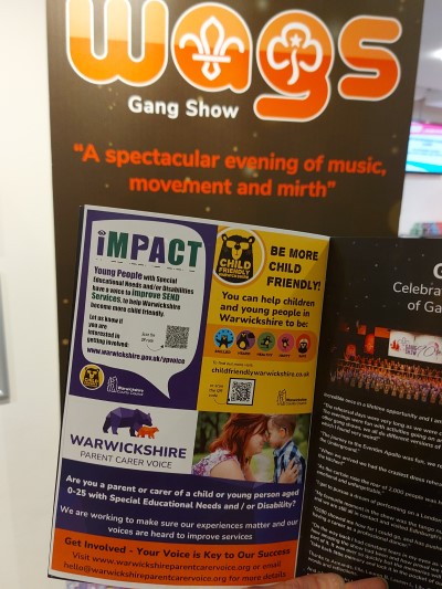 A photo of a CFW advert next to an advert for the SEND IMPACT Youth Forum and Warwickshire Parent Carer Voice in the WAGS brochure, in front of a WAGS banner.