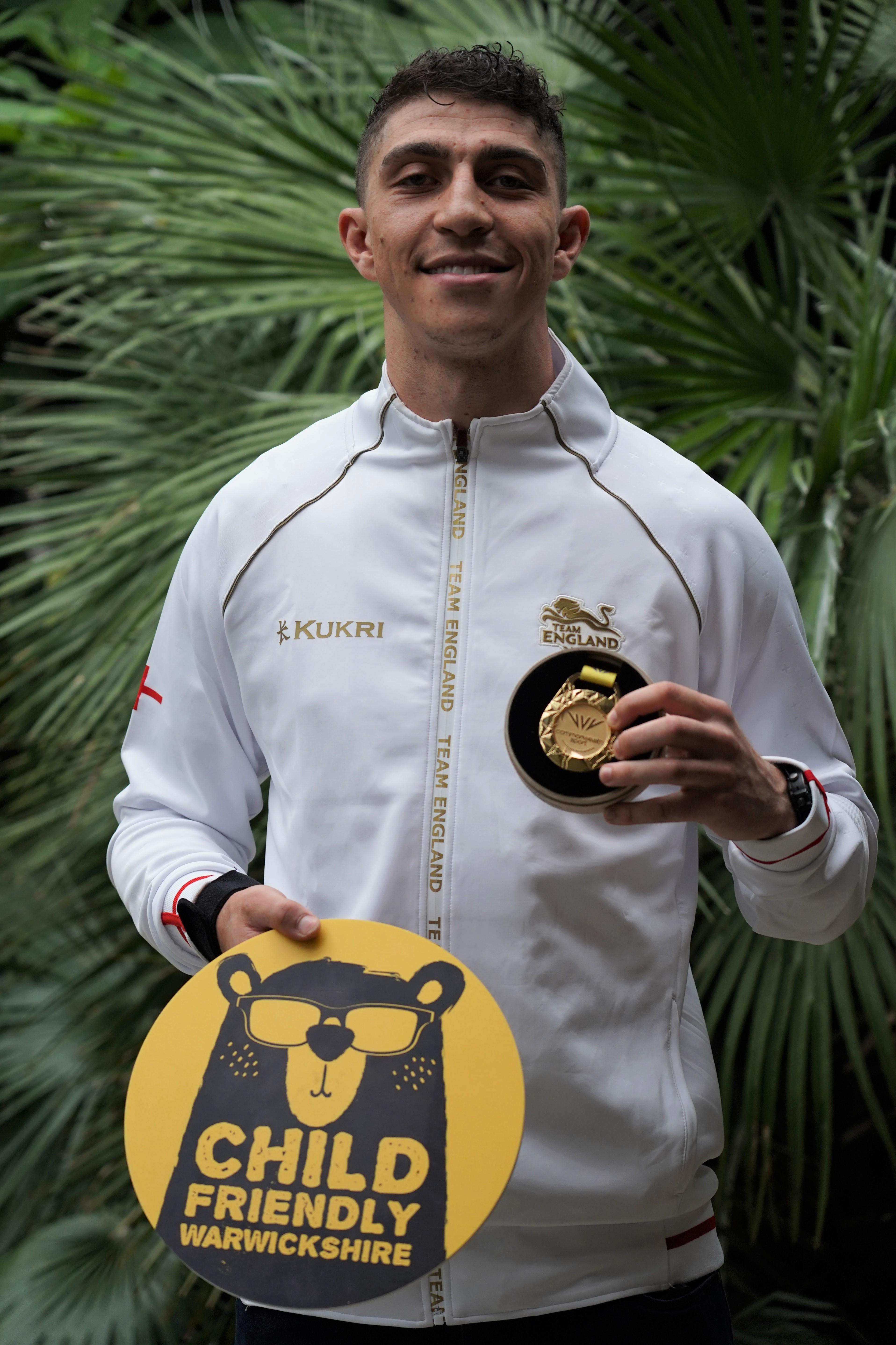 Lewis Williams in his England uniform with his gold medal, holding the CFW logo