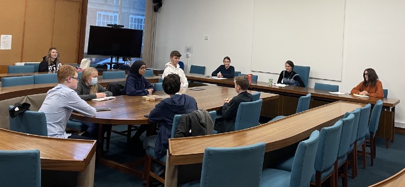 9 children sat in a council meeting room. Holding a meeting of the young council.